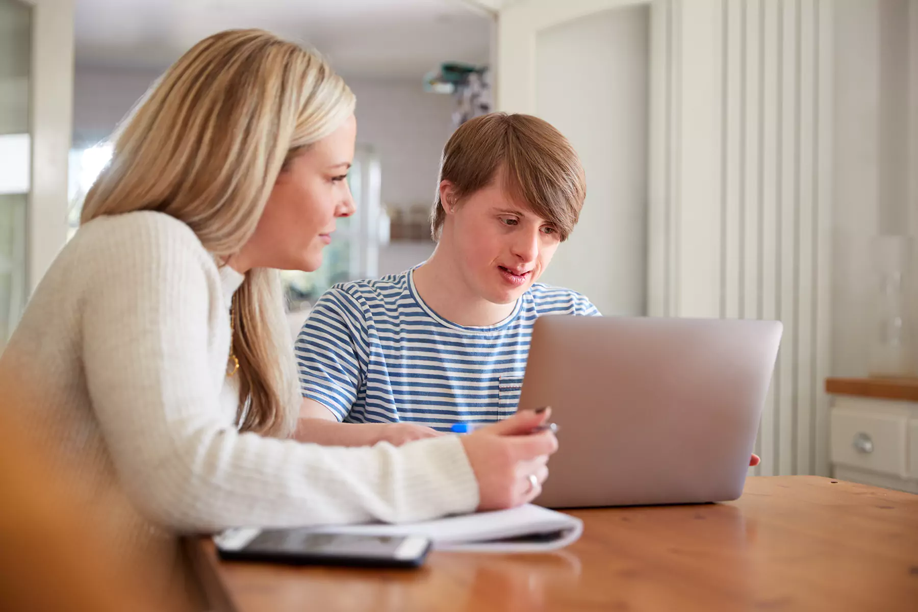Disabled man with down syndrome looking at laptop with support worker