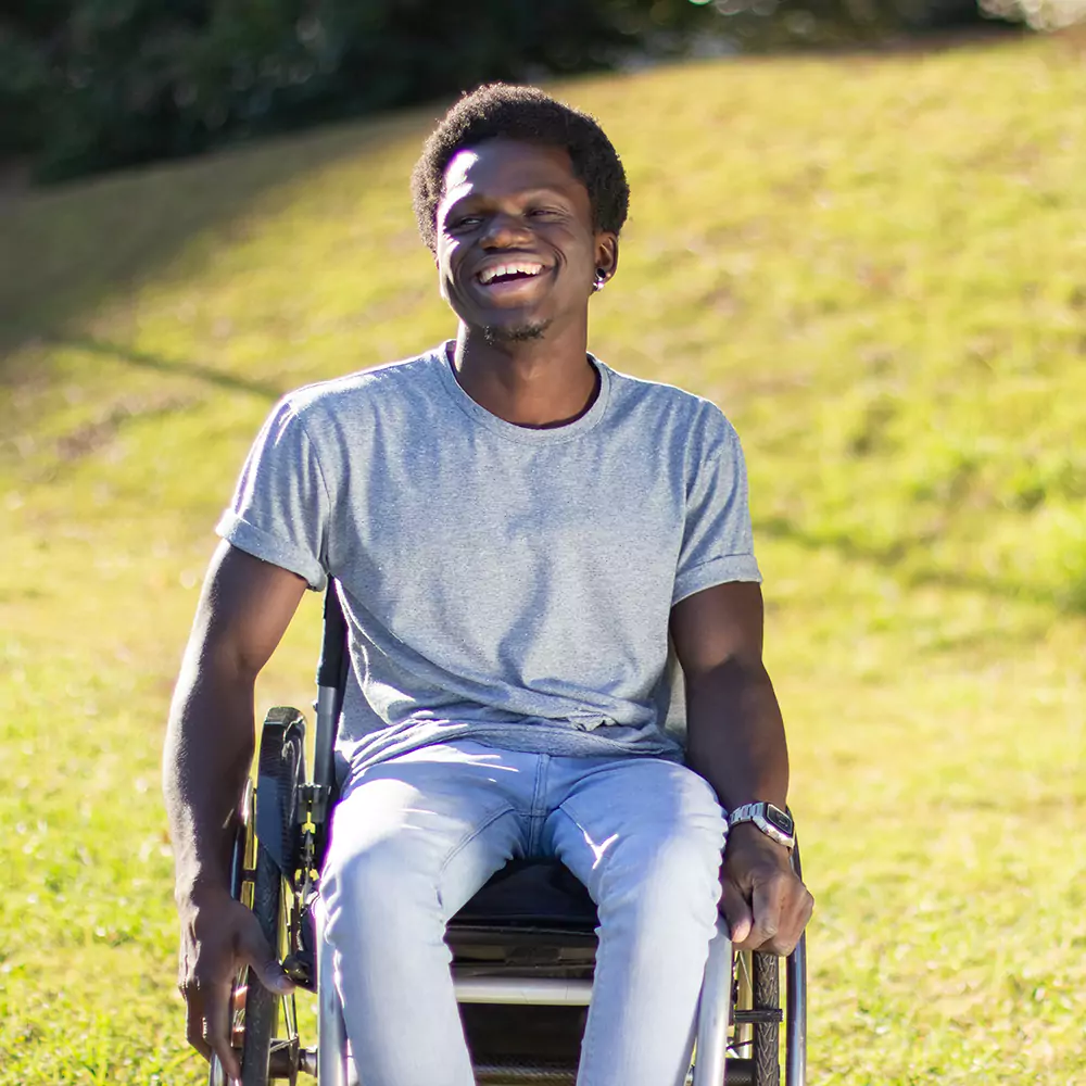 Disabled man smiling happily in wheelchair while sitting outside in park